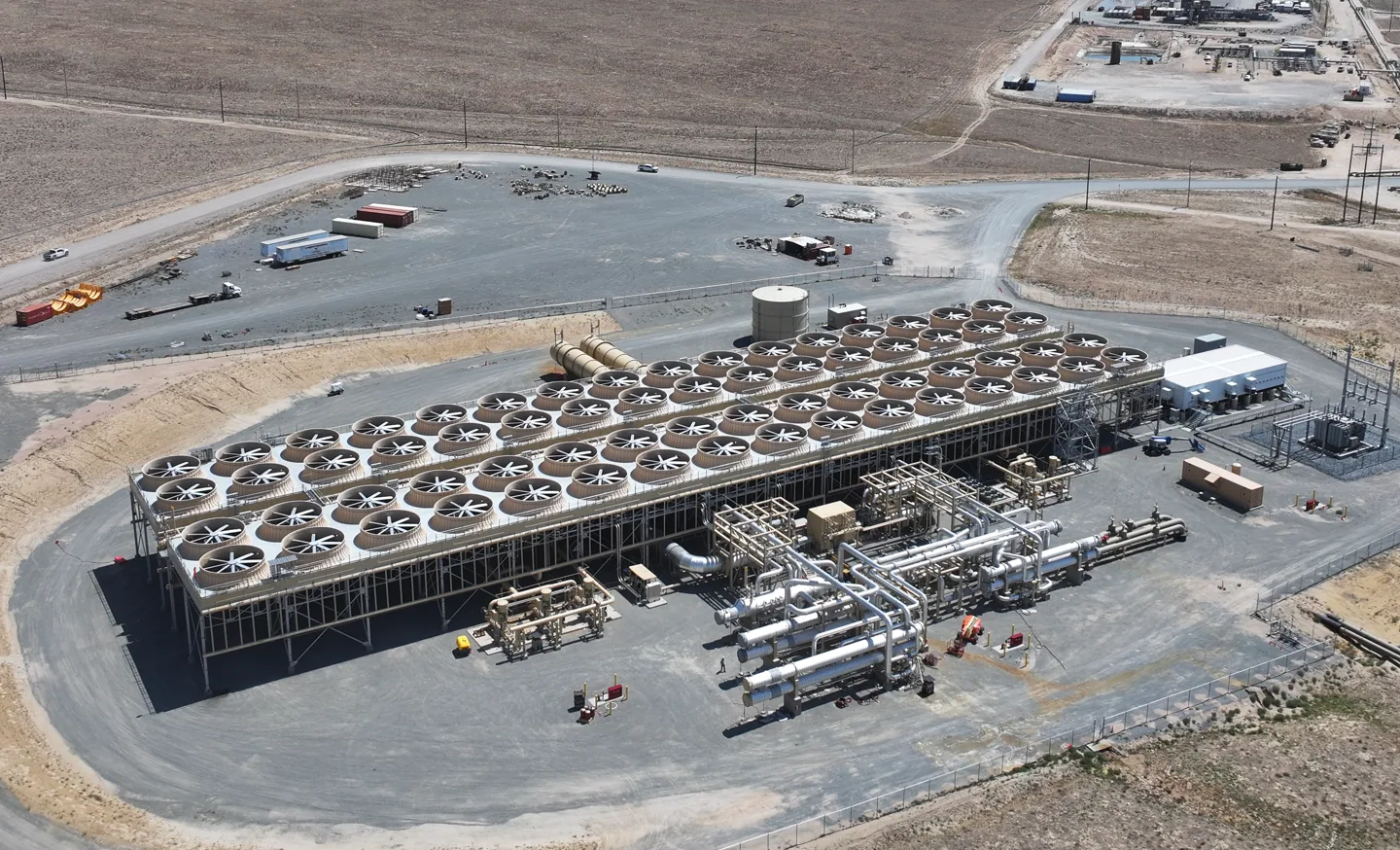 An aerial view of the Fervo Energy Cape Station geothermal power plant in Utah, featuring a large array of cooling fans and piping.