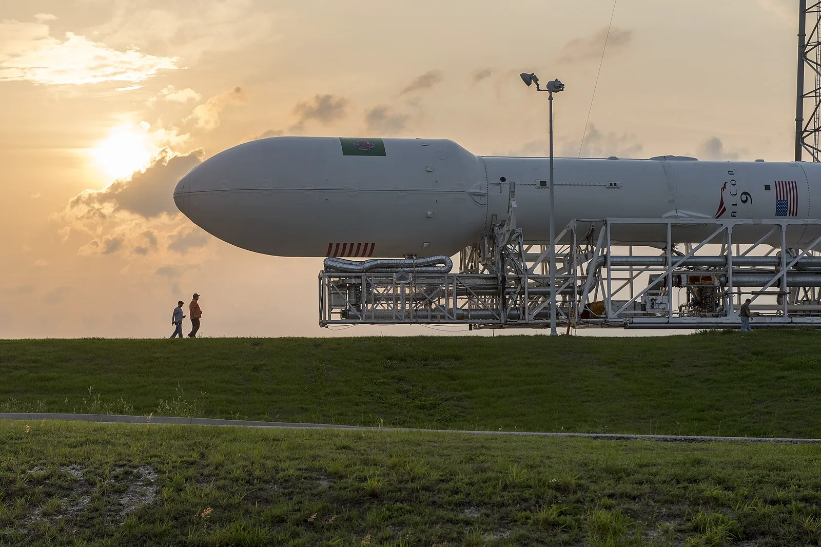 A SpaceX Falcon 9 rocket lies horizontally on its transporter erector against a sunset sky.