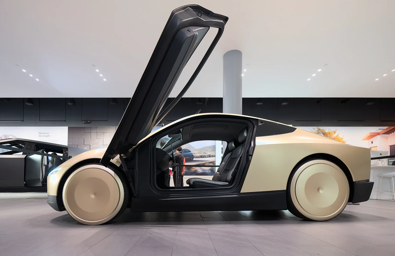Side view of a gold Tesla Cybercab with its butterfly door open inside a showroom.