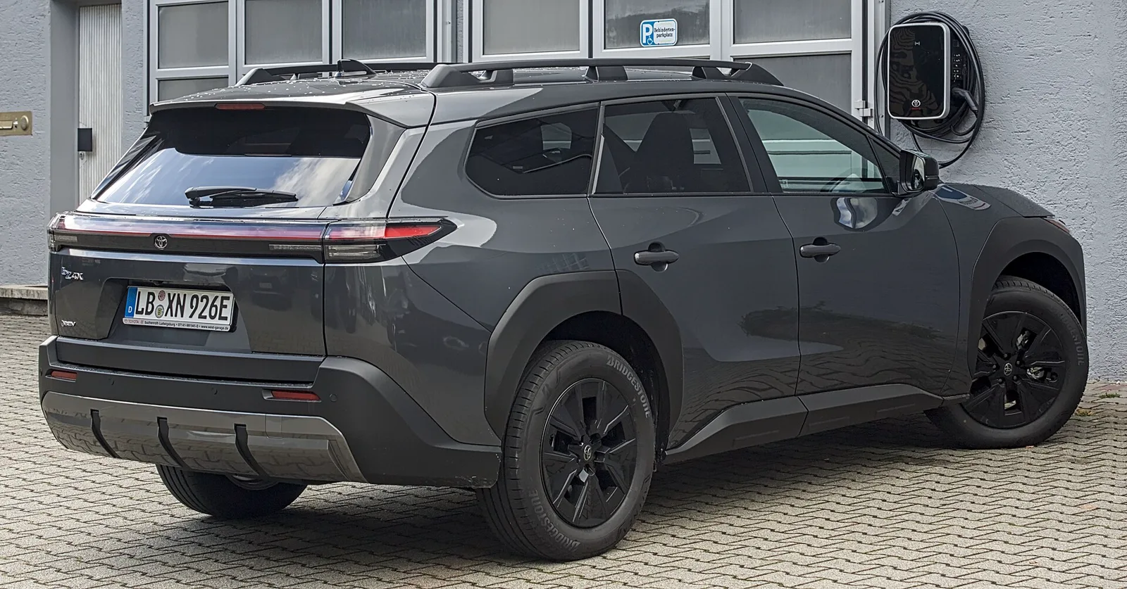 A dark gray Toyota bZ4X electric SUV parked in front of a building next to a charging station.