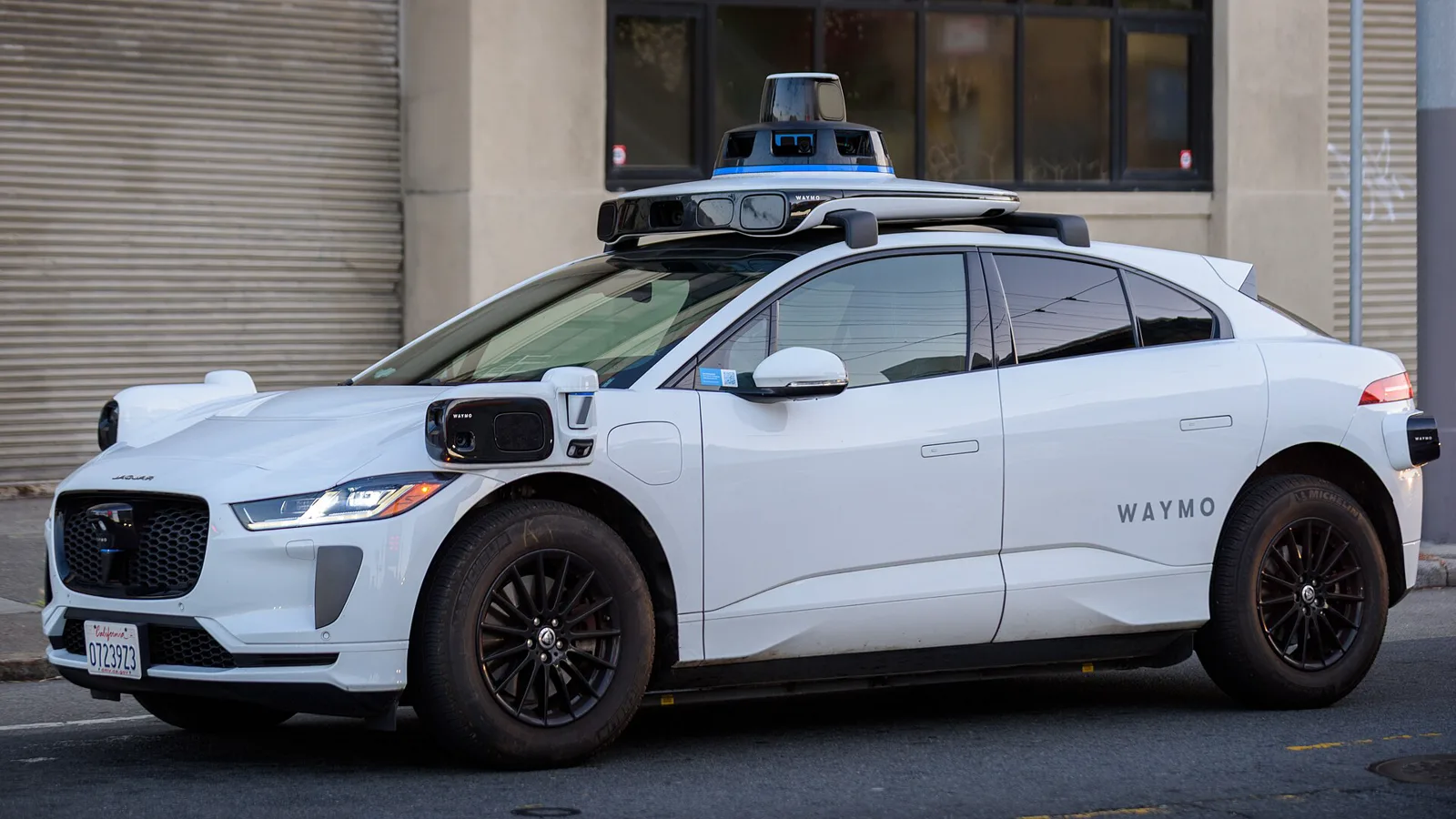 A white Waymo Jaguar I-PACE autonomous vehicle parked on a city street.